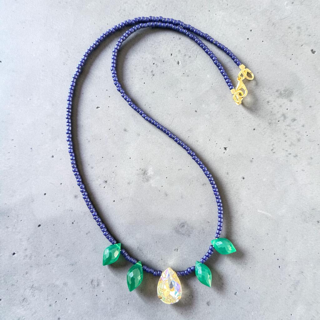 Necklace with blue beads and green teardrop-shaped pendants on a gray surface