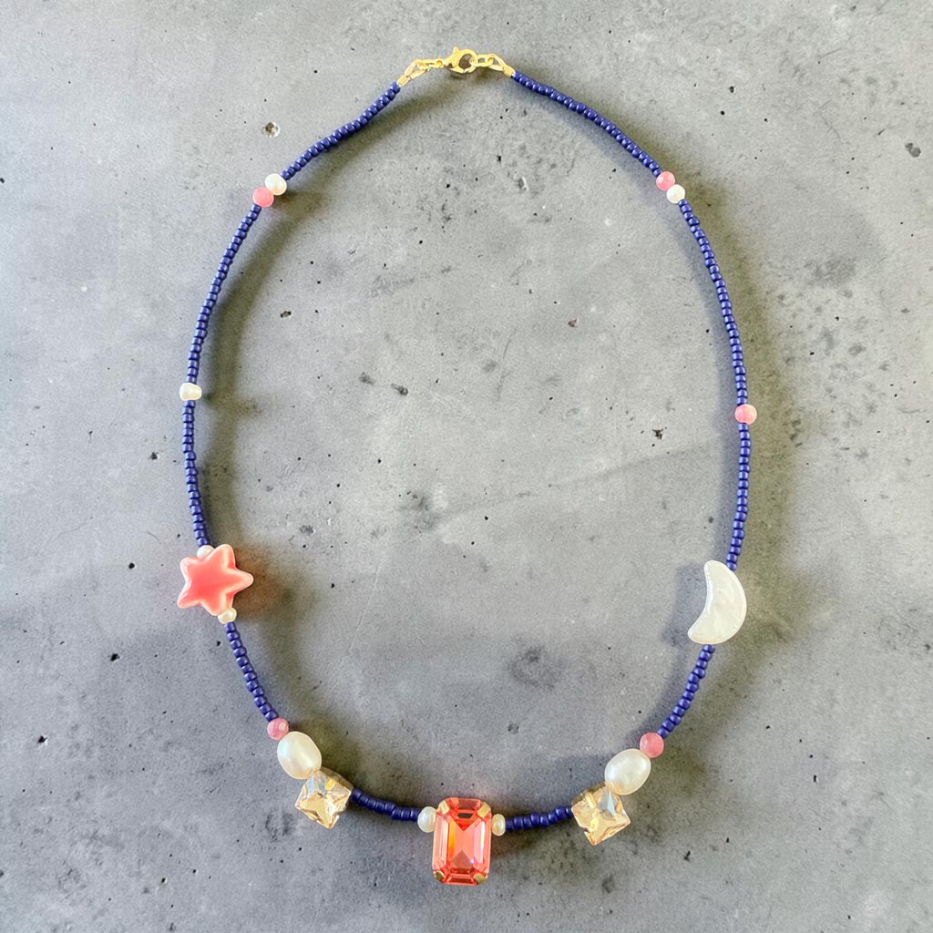 A handcrafted celestial-inspired necklace featuring a delicate arrangement of a real pearl moon, ceramic star charm, natural pearls, crystals, and carefully selected natural stones.